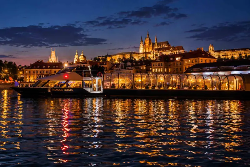 Večerní Praha a osvětlená skleněná loď na Vltavě